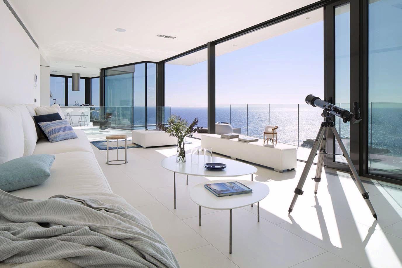 Bright, modern living room with ocean view, white walls, large windows, telescope, and white sofas.