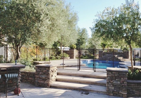 Stone patio with pool, surrounded by trees and a black fence.