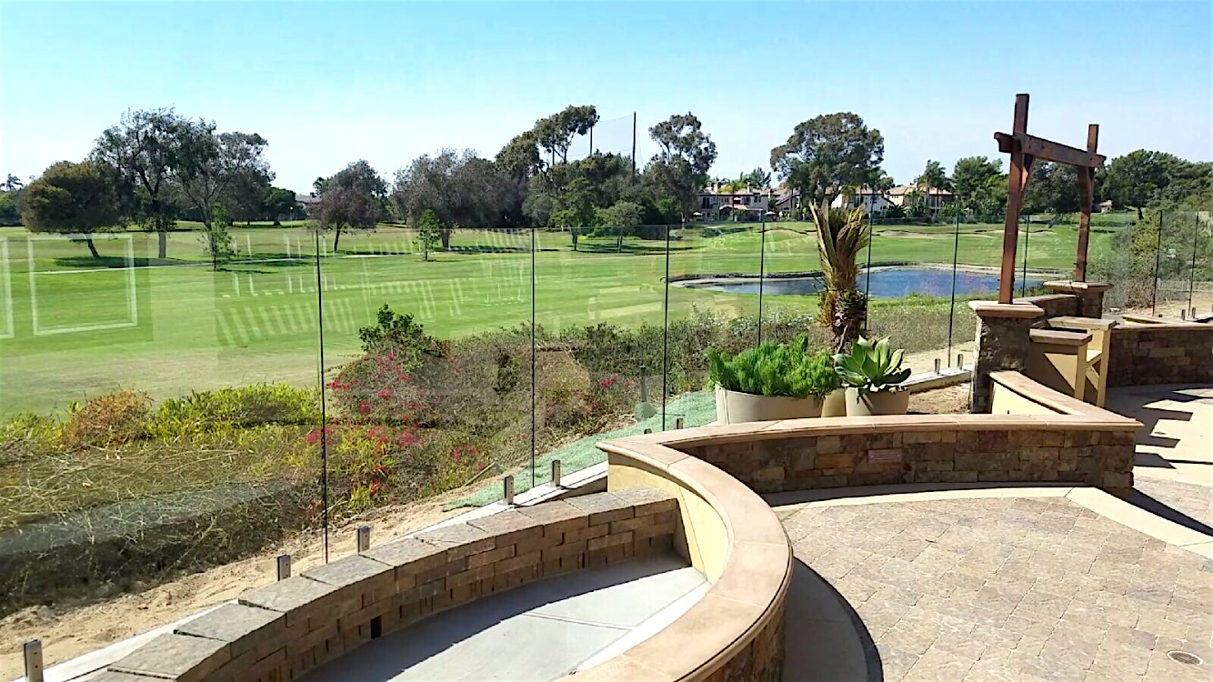 View of a golf course with green grass, trees, and a small pond, seen from a stone patio.