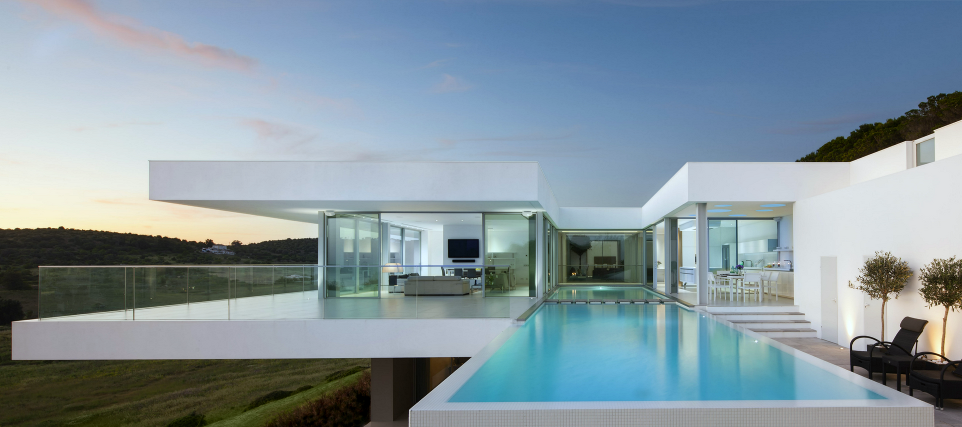 Modern white house with pool overlooking a landscape, clear blue sky.
