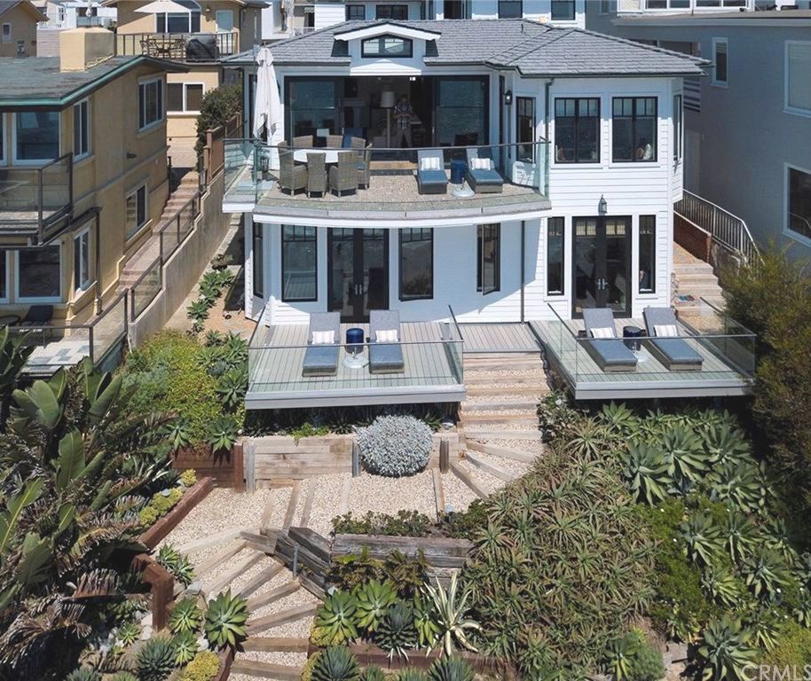 White beachfront house with decks, stairs, and lush landscaping. Ocean views.