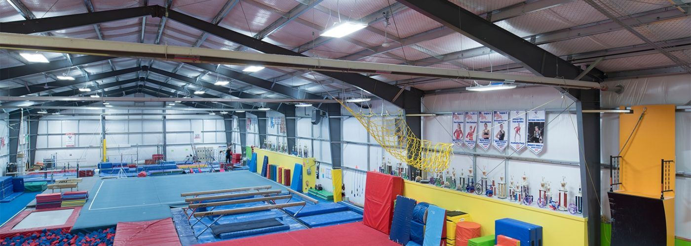 Gymnasium interior with mats and equipment, featuring a high ceiling with support beams.