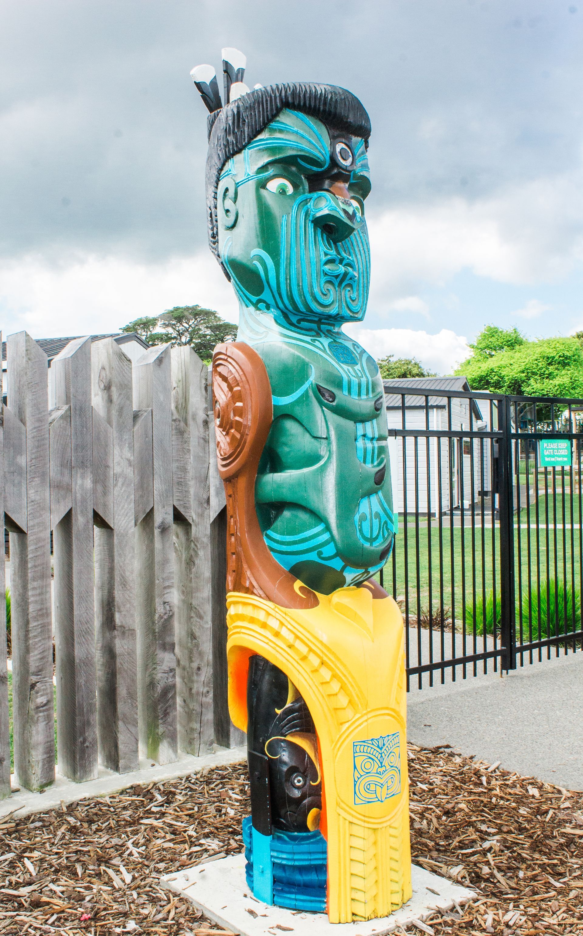A statue of a man is sitting on a yellow chair in front of a wooden fence.