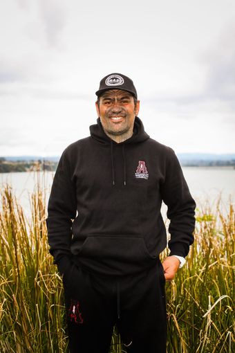 A man in a black hoodie and hat is standing in a field of tall grass.