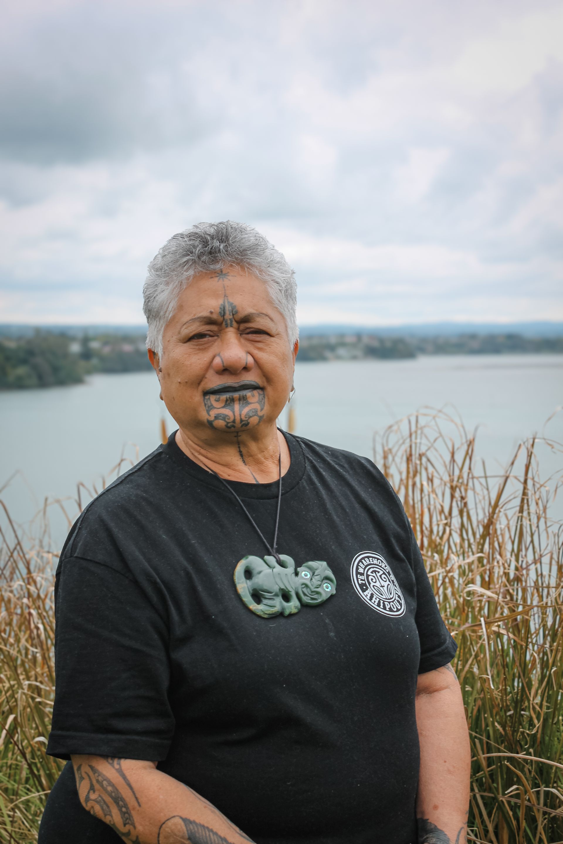 A woman with a tattoo on her face is standing in front of a body of water.