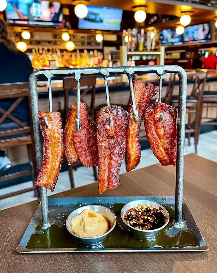 A bunch of bacon is hanging from a rack on a table.