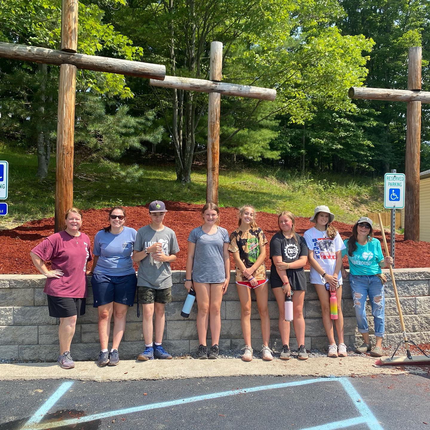 A group of eight people stand in a line in front of three large wooden crosses on a hill.