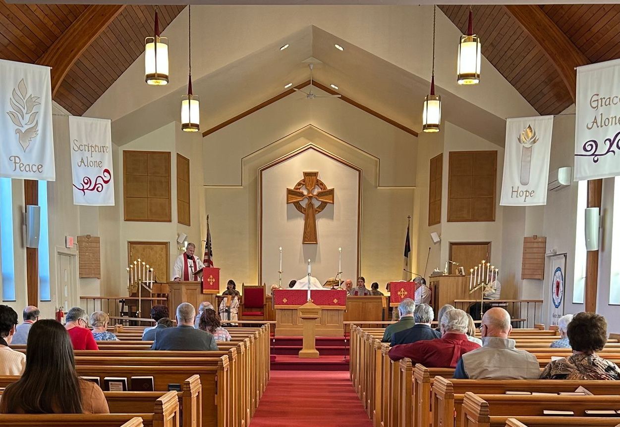 Interior view of a church sanctuary with wooden pews, a central altar featuring a wooden cross, and banners on the walls.
