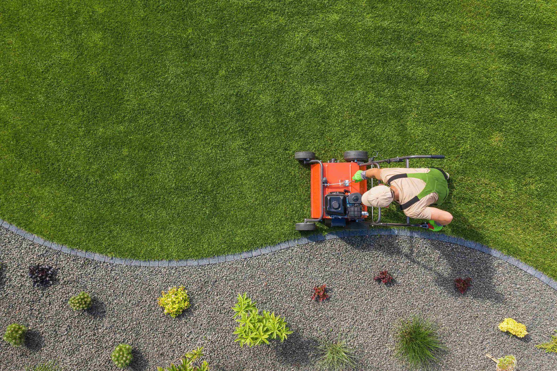 Gardener mowing a curved lawn edge beside a gravel flower bed