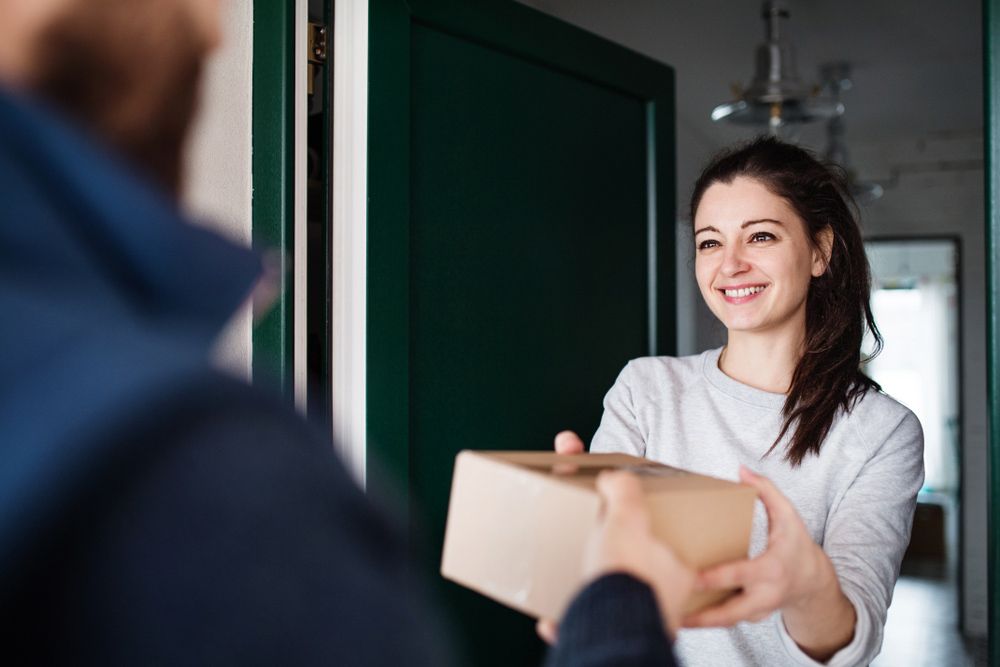 A Woman Is Receiving A Package From A Delivery Man At Her Door — Express City Couriers in Bungalow, QLD