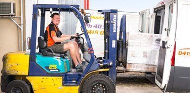 A Man Is Driving A Forklift Next To A White Van — Express City Couriers in Bungalow, QLD