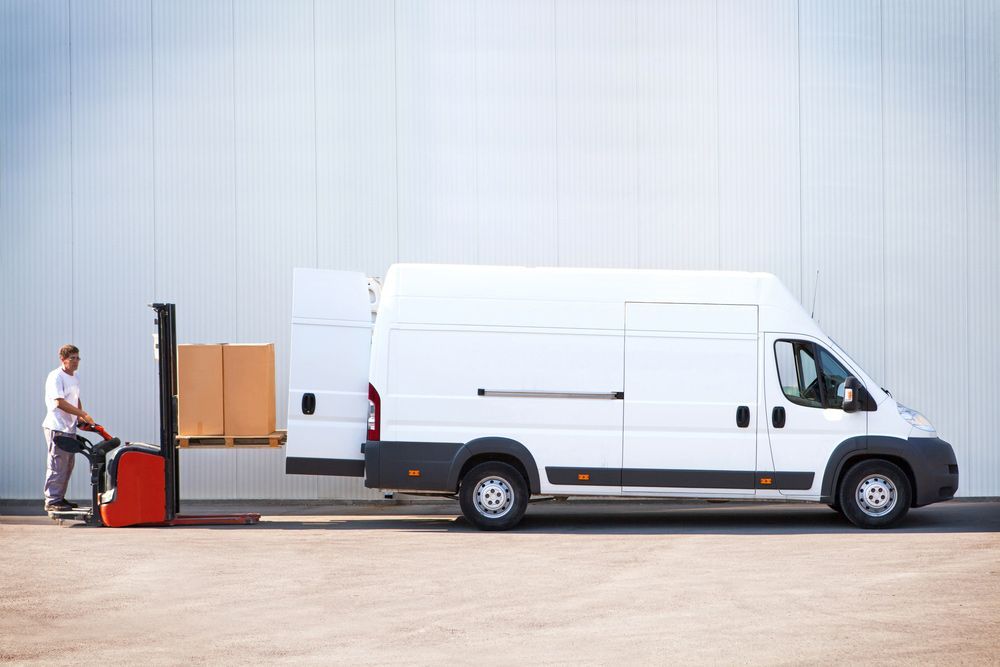 A Man Is Loading Boxes Into A White Van With A Forklift — Express City Couriers in Cairns, QLD