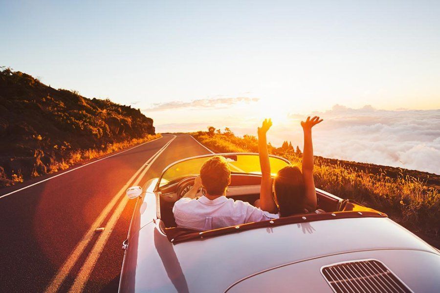 A man and a woman are driving down a road in a convertible car | Superior Auto Care