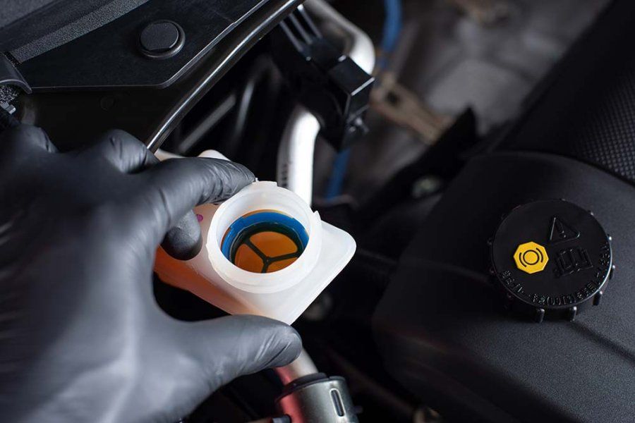 A person wearing black gloves is pouring brake fluid into a bottle | Superior Auto Care