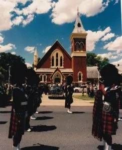 A group of bagpipe players are marching in front of a church.