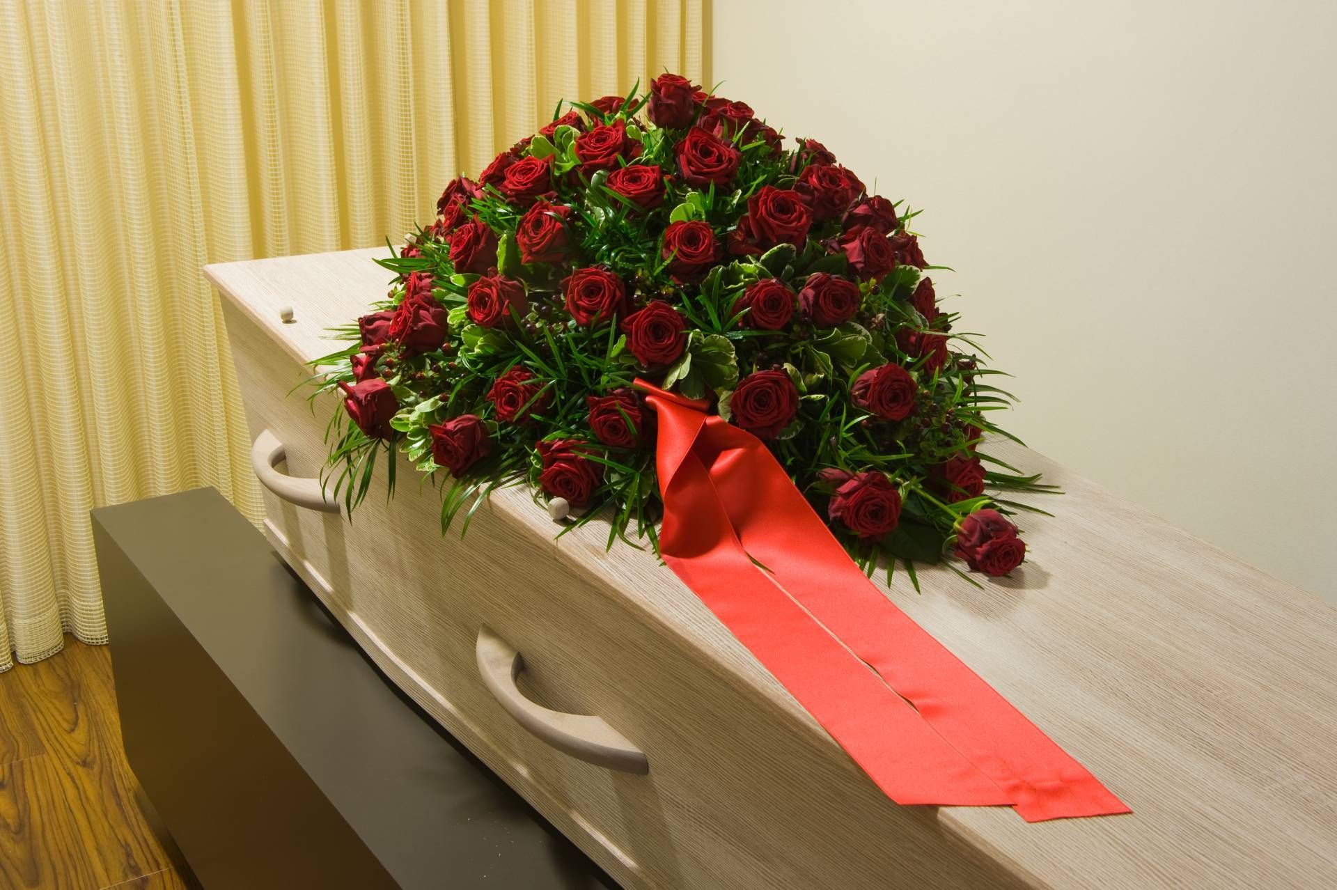 a coffin with red roses and a red ribbon on it.
