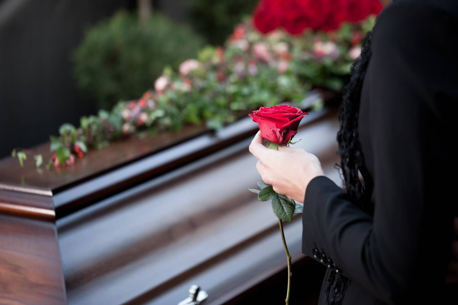 a woman is holding a red rose in front of a coffin.