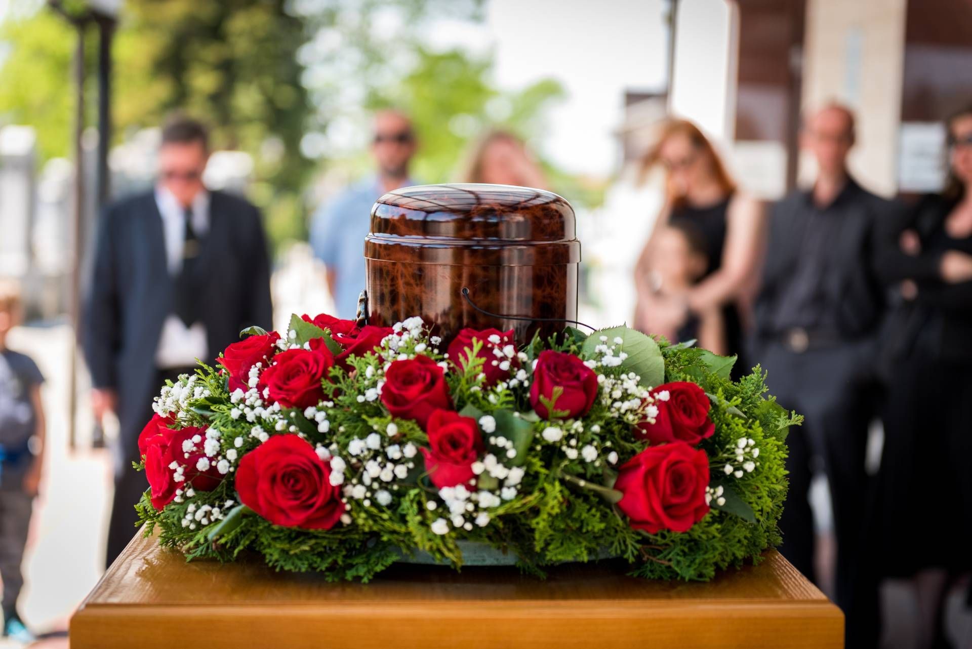 a wooden urn surrounded by red roses and baby 's breath at a funeral.