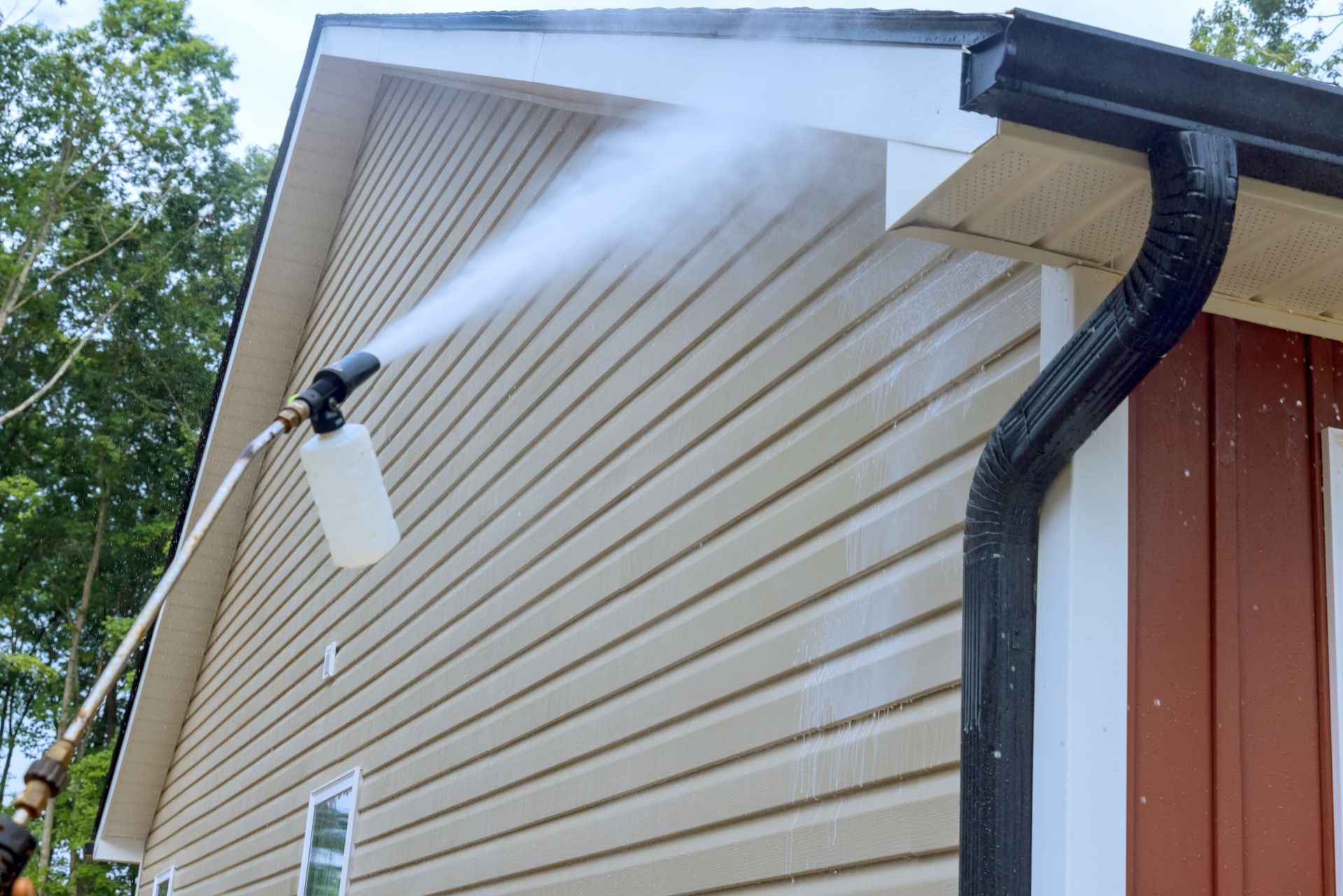 A man is using a high pressure washer to clean the side of a house.