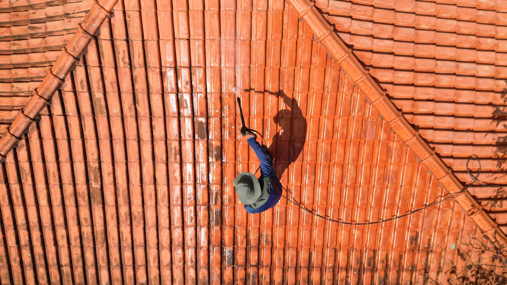 An aerial view of a man cleaning a tiled roof with a pressure washer.