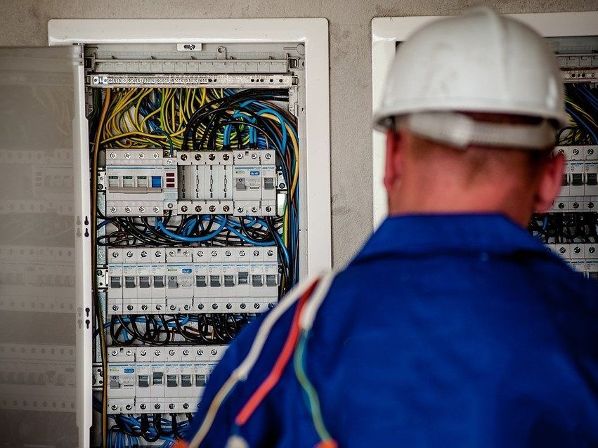 A man wearing a hard hat is looking at an electrical box.