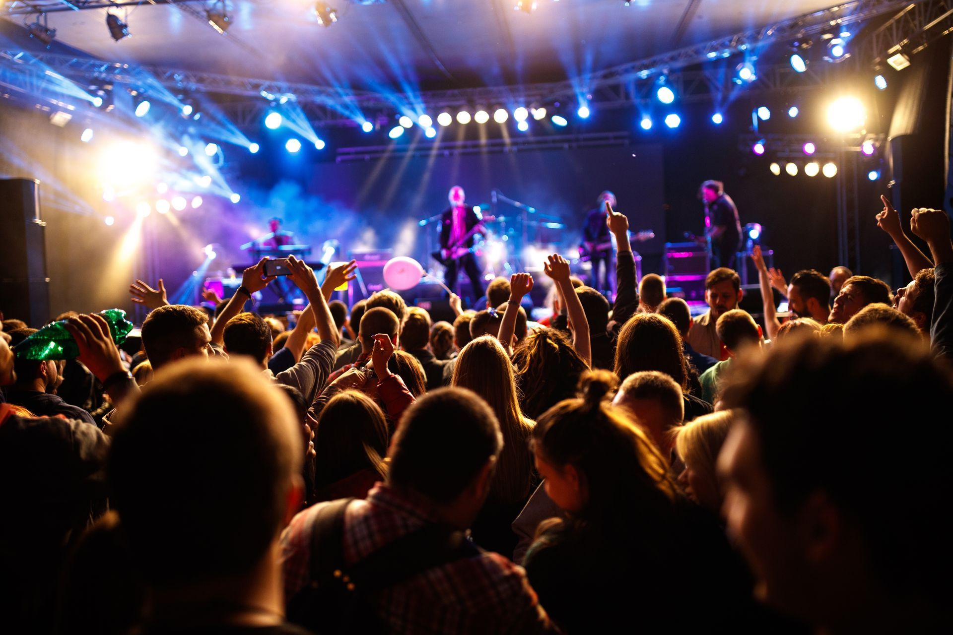 Crowded concert venue with a cheering audience and bright blue and purple stage lights