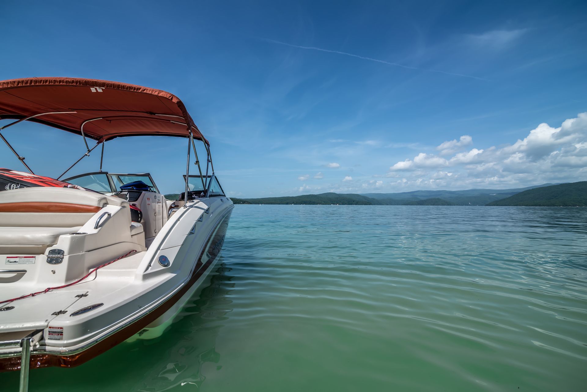White speedboat with red canopy on calm green water under a blue sky, near distant hills