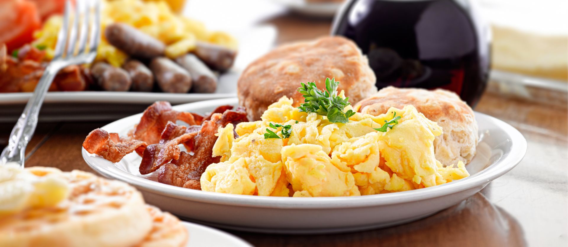 Plate of scrambled eggs, bacon, toast, and coffee on a breakfast table