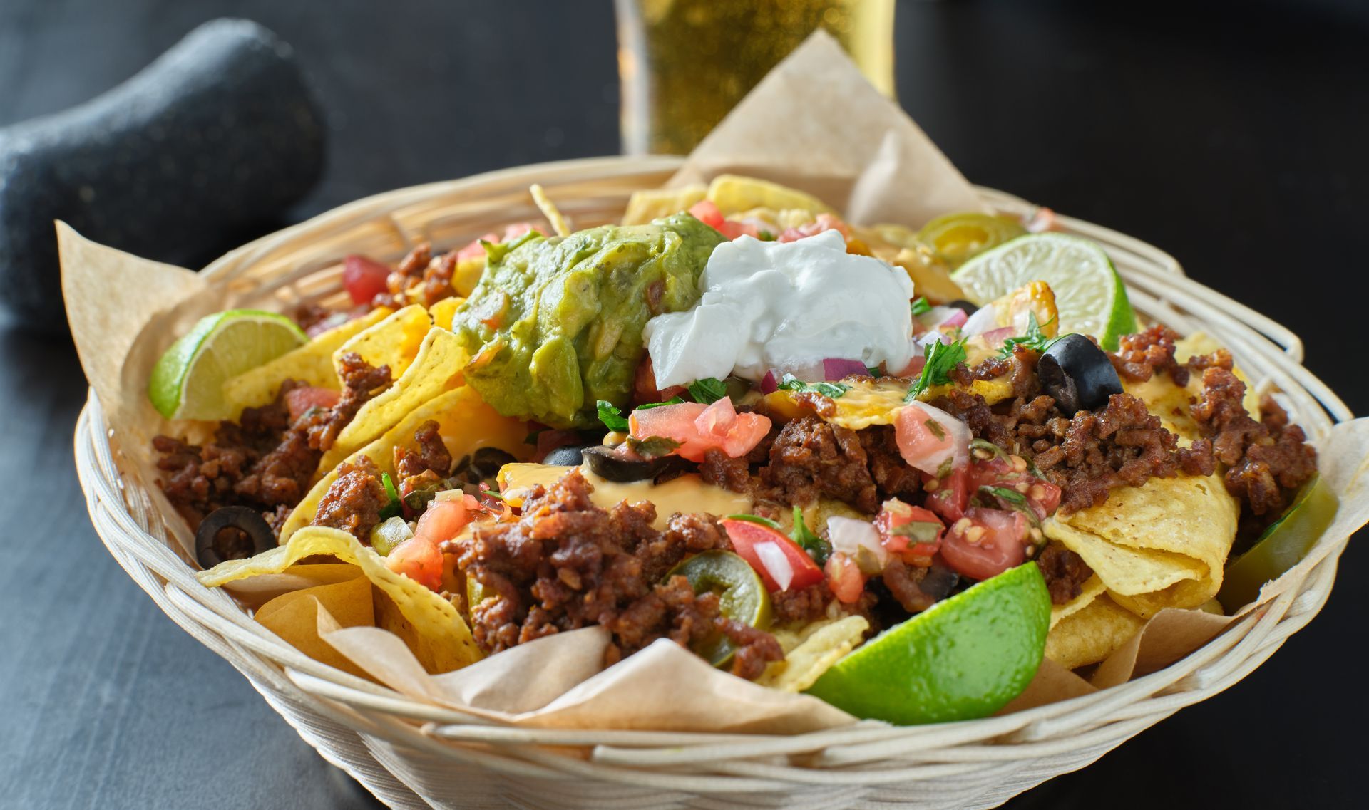 Basket of loaded nachos with beef, guacamole, sour cream, pico de gallo, and lime wedges