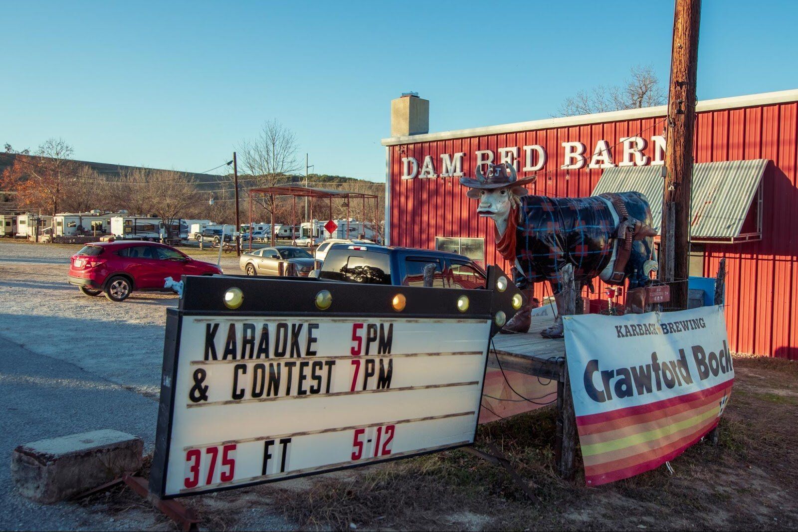 Signs outside a red barn advertise karaoke, contests, and Crawford Rocker in a parking lot.