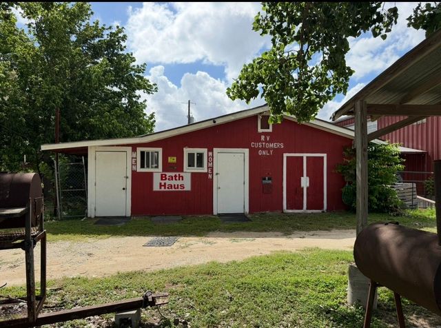 Red barn-style building with white trim and doors, surrounded by trees and grass under a blue sky.