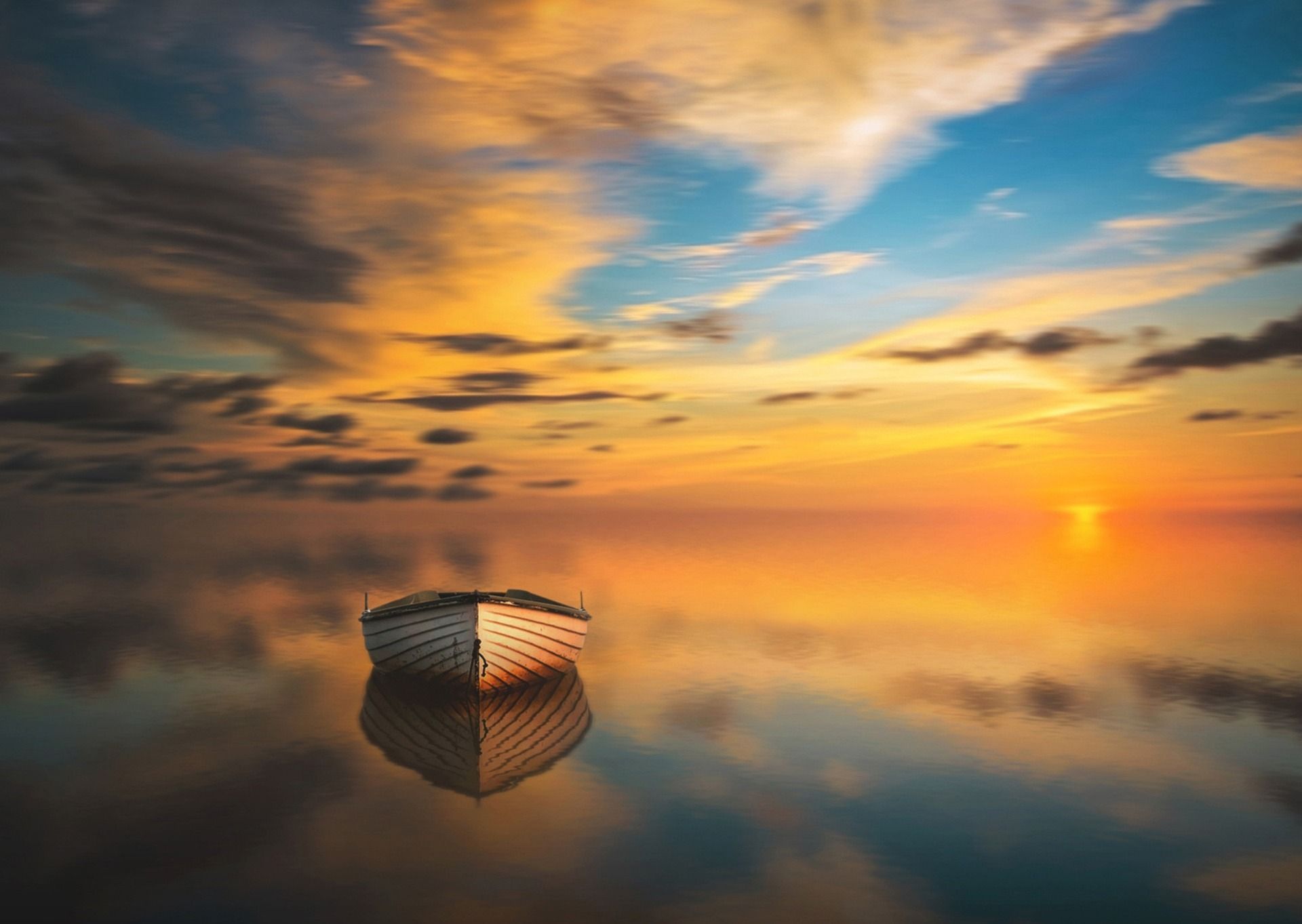 Boat on calm water at sunrise, with golden clouds reflected in the mirror-like surface.