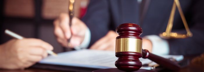 a man holding a pen, signing a document With a gavel on the desk.