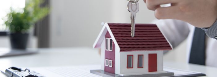 Small model house with a person handing over a set of keys, symbolizing landlord-tenant housing rights and rental agreements