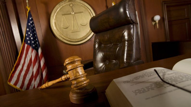 Court room showing judge's chair, American Flag, gavel, and scales.