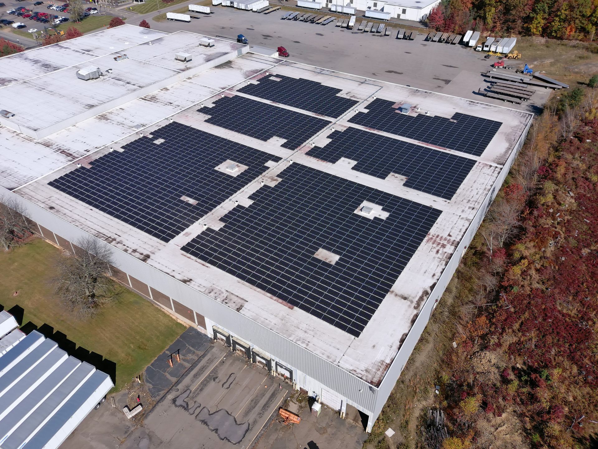 Aerial view of a commercial building roof with large sections of black solar panel arrays installed on a light surface.