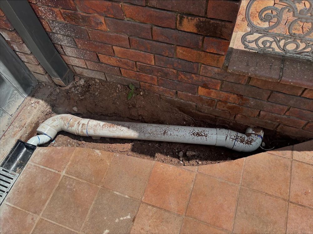 A Pipe is Sitting in the Dirt Next to a Brick Wall — Otto’s Plumbing & Gasfitting in McDowall, QLD