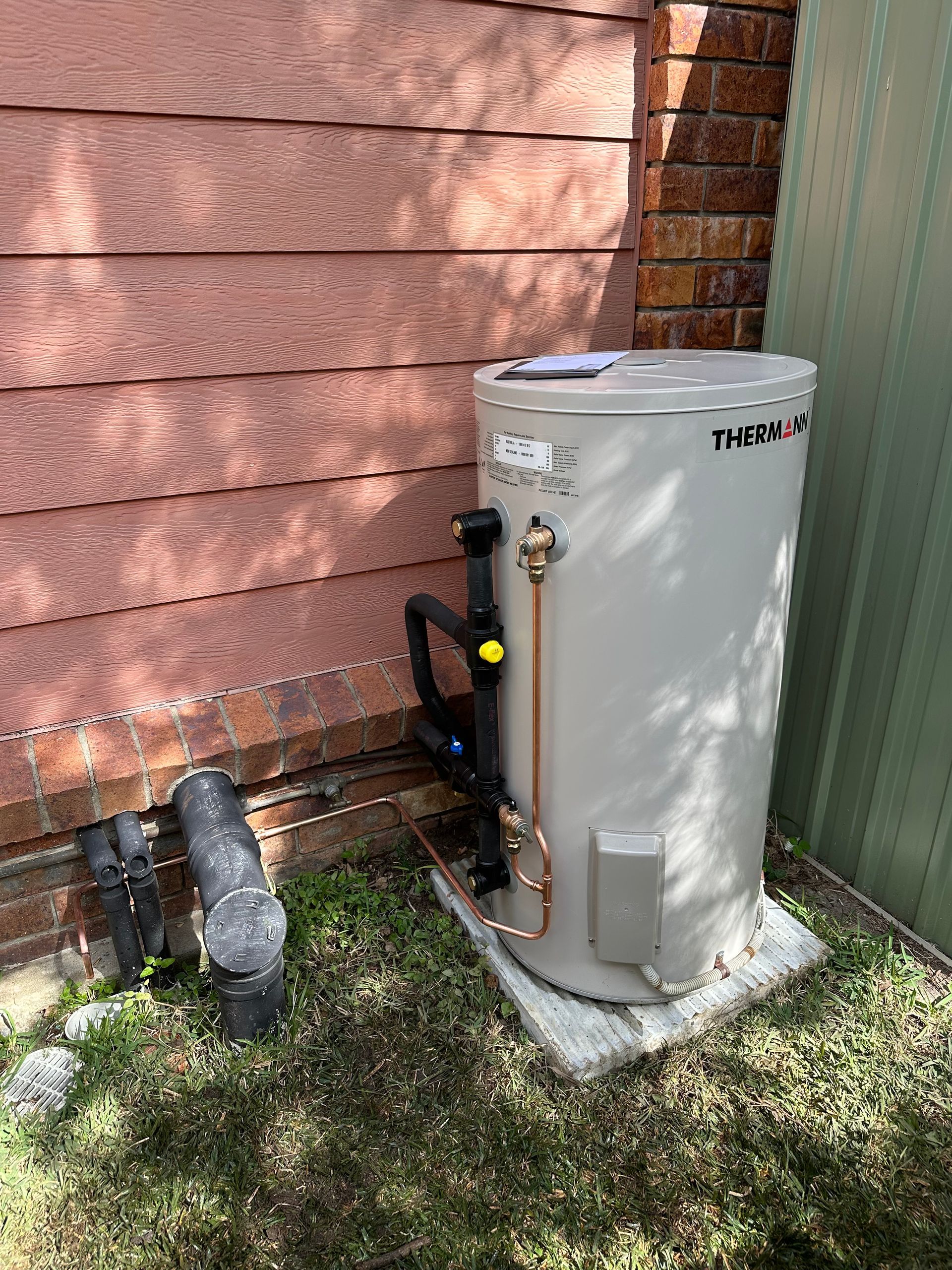 A Hot Water System Is Sitting Outside A House — Otto’s Plumbing & Gasfitting in McDowall, QLD