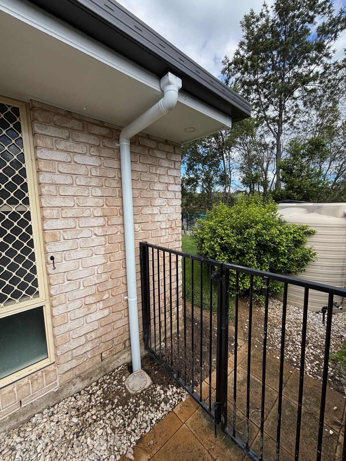A White Pipe Runs Downs The Side of a Brick House — Otto’s Plumbing & Gasfitting in McDowall, QLD
