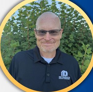A bald man with a beard and glasses is wearing a black polo shirt.