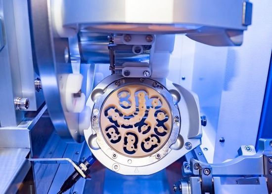 A close-up of a dental milling machine, carving a crown from a beige ceramic block.