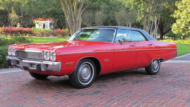 Red classic car parked on a brick driveway beside a garden