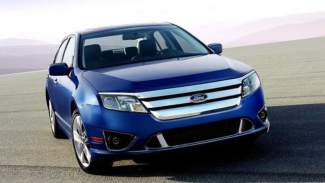 Blue Ford sedan driving on a road in a desert-like landscape