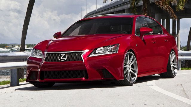 Red Lexus sports sedan parked on a sunny road near palm trees and the beach.