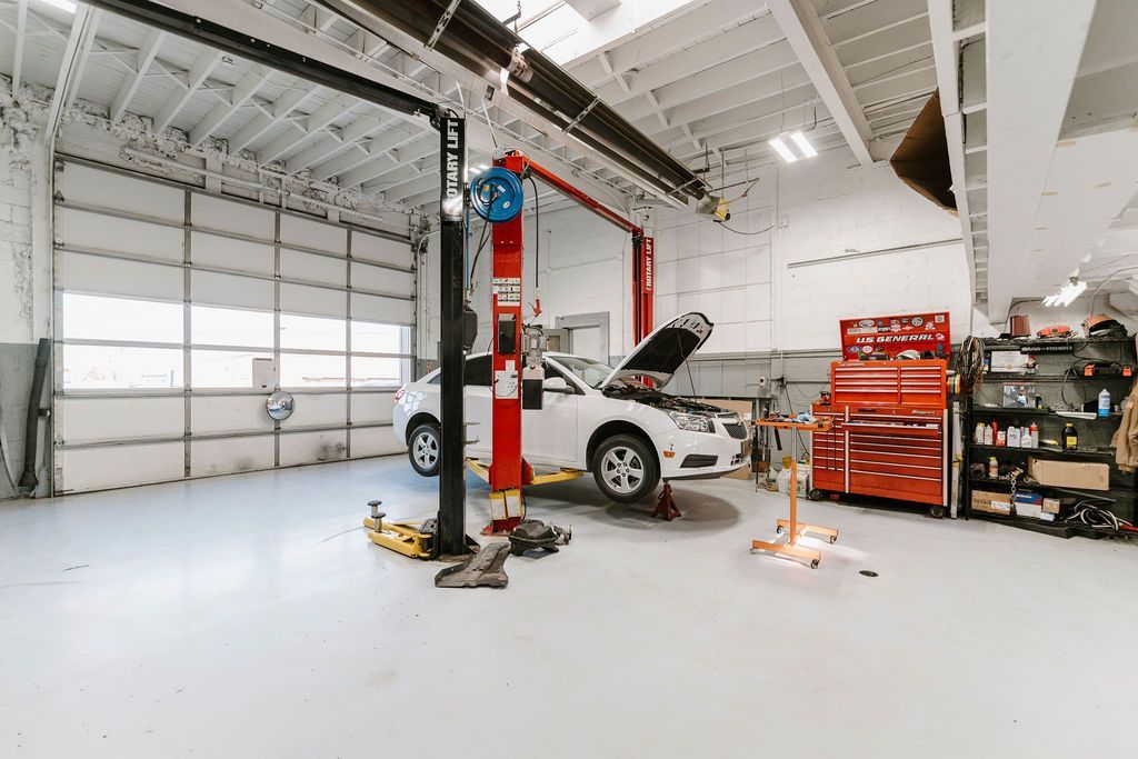 Auto repair shop with a car on a lift, tool cabinets, and a large garage door in a bright white workshop