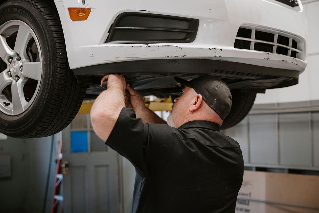 Mechanic working under a raised white car in an auto repair shop