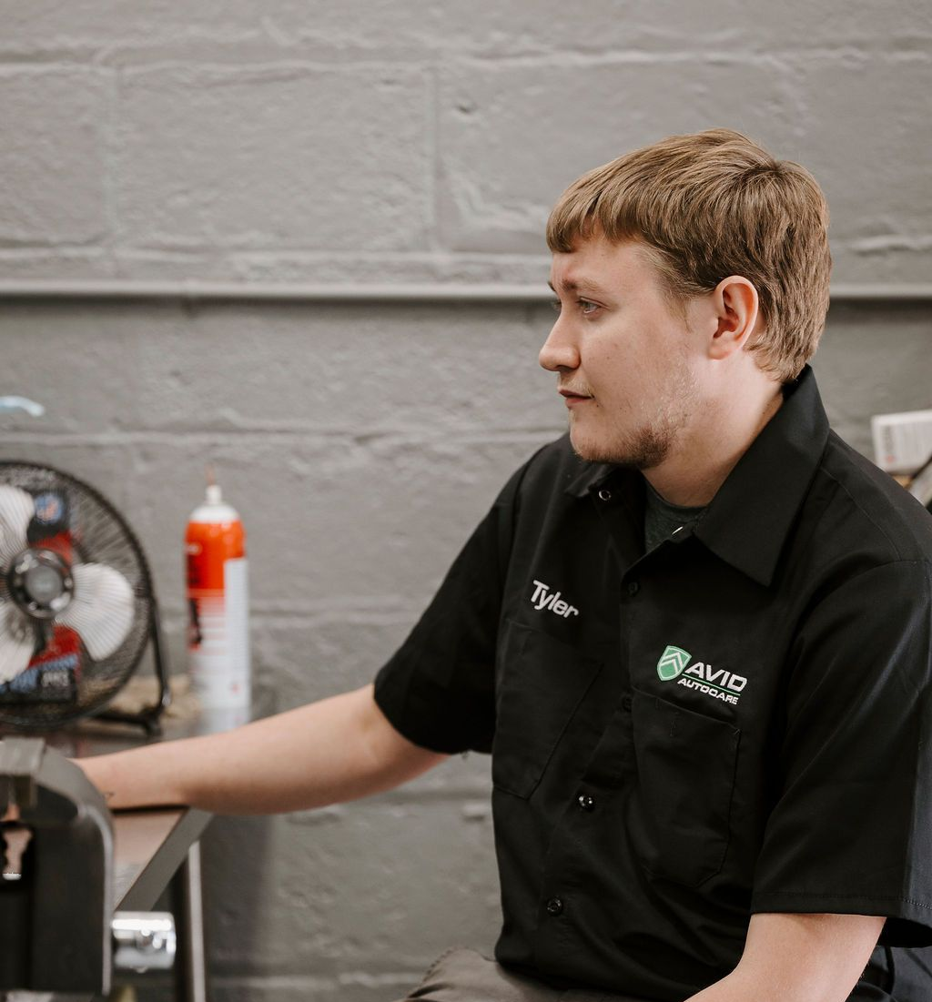 Person in a black work shirt seated at a desk in a workshop, looking right.