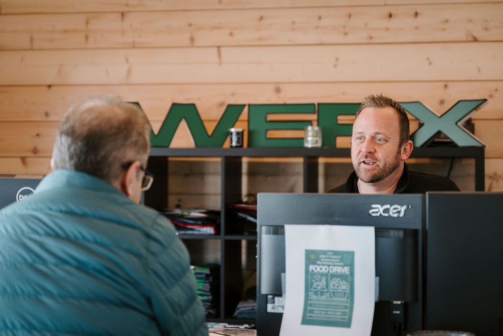 Two people talking at a computer counter in an office with a wooden wall and green 