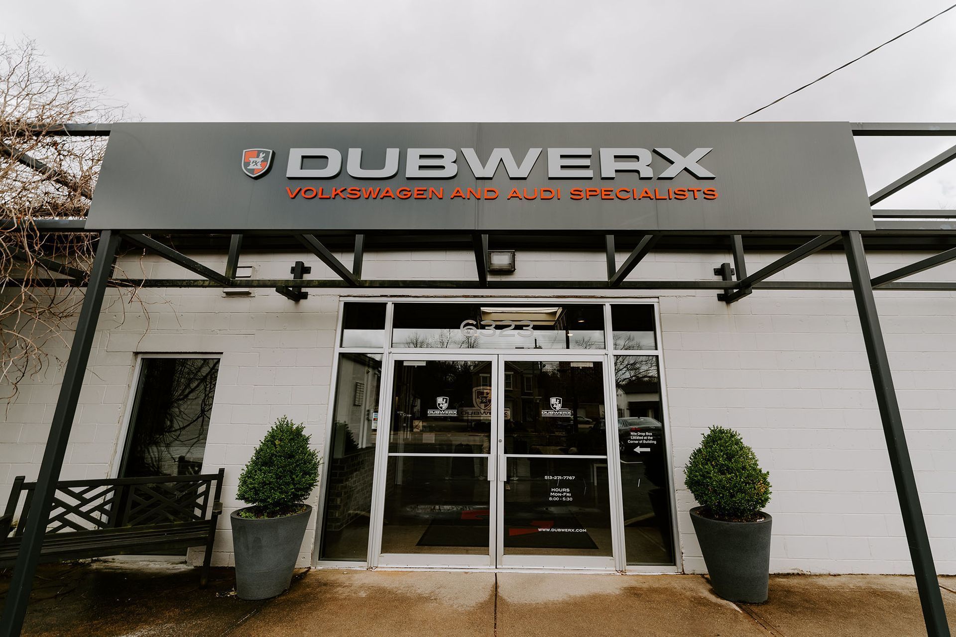 Front entrance of Dubwerx automotive shop with gray sign, glass doors, and potted plants