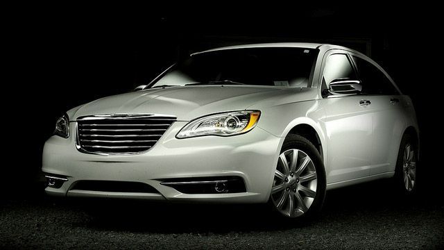 Silver luxury sedan on a dark background, front-left view, headlights on.